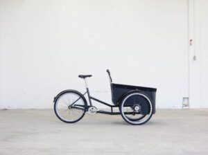 Side view of a three-wheeled cargo bike in a minimalistic indoor setting.